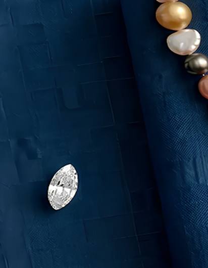 Gold necklace with diamond pendant on blue satin, surrounded by loose gemstones